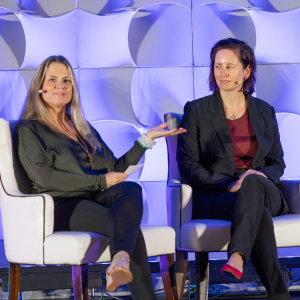 A photo of two women in business attire sitting and speaking onstage during a panel discussion