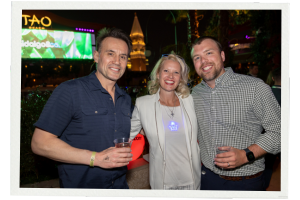 A photo of three people, a woman and two men, smiling for the camera at a Channel Partners networking event at TAO beach club in Las Vegas. 